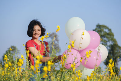 Happy girl with flowers on field against sky