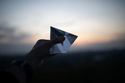 Cropped hand holding crystal against sky during sunset