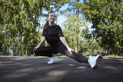 Girl in sportswear on a sunny summer day on the embankment in the park doing fitness and stretching