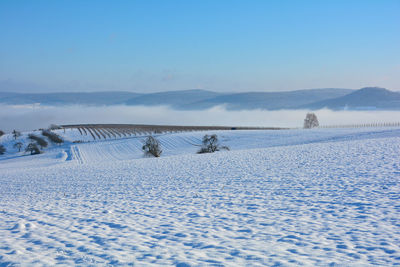 Snow landscape with fields and fog in the valley and with blue sky in spessart, bavaria, germany