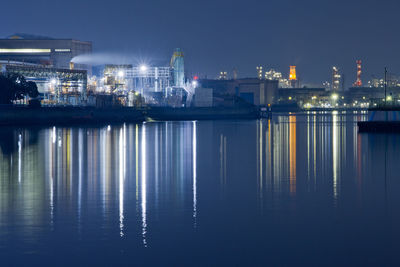 Illuminated city by sea against sky at night