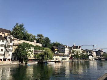 Buildings by river against clear sky