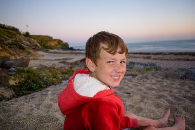 Portrait of smiling boy on beach against sky during sunset