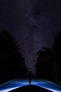 Rear view of silhouette man standing on road against sky at night