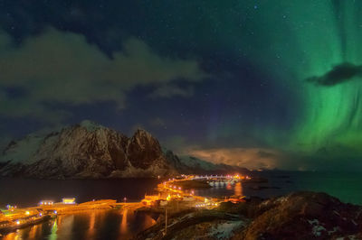 Illuminated city by sea against sky at night