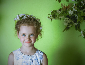 Portrait of girl wearing flowers while standing against wall