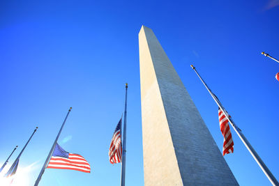 Low angle view of washington monument and american flags against blue sky