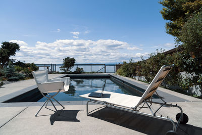 Summer home office, chair and chaise lounger by the pool with laptop computer, mid day sun.