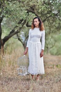 Bride holding birdcage while standing against trees