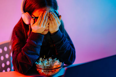 Girl covering eyes with popcorn on table