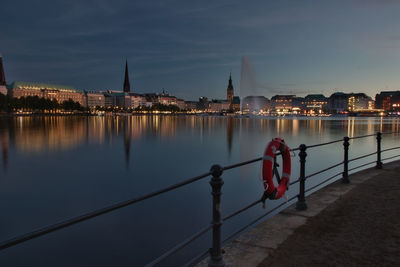 Illuminated city by river against sky at night