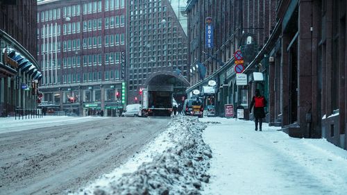 Snow covered road amidst buildings in city