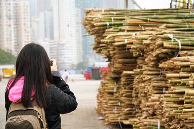 Rear view of woman photographing stacked bamboos 