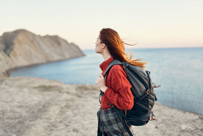 Young woman standing at beach against sky