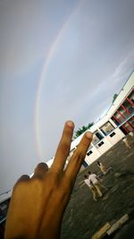 Low angle view of hand holding rainbow against sky