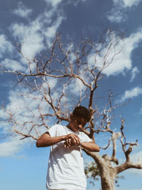 Low angle view of boy standing by tree against sky