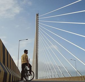 Rear view of man riding bicycle on bridge against sky