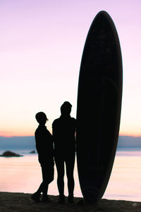 Silhouette couple standing by sea against sky during sunset