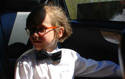 Boy wearing bow tie sitting in car during sunny day