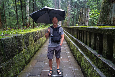 Portrait of man standing on wet footpath holding umbrella