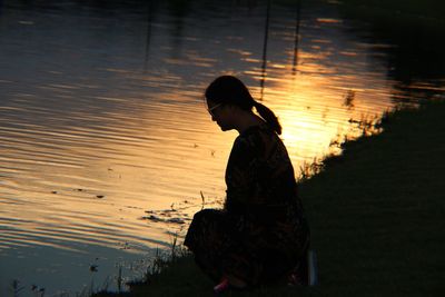 Silhouette woman kneeling by lake during sunset