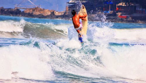 Full length of shirtless man splashing water in sea