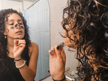 Woman peeling off black facial mask of her face in the bathroom.