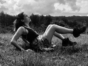 Young woman looking away while sitting on field