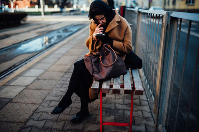 Full length of man using mobile phone while sitting on footpath