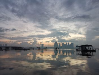 Silhouette buildings by sea against sky during sunset