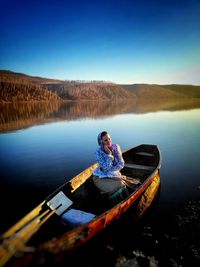 Man sitting on boat in lake against clear blue sky