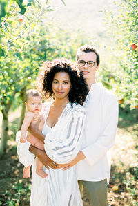 Portrait of smiling couple carrying baby while standing outdoors