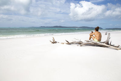 Man sitting on beach against sky