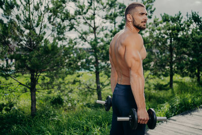 Side view of shirtless man lifting dumbbells in park