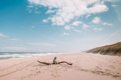Toddler sits on driftwood on beach