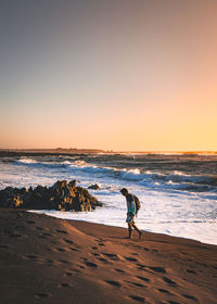 Man walking at beach against clear sky during sunset