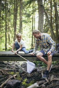 Smiling daughter holding bottle in fishing net by father in forest