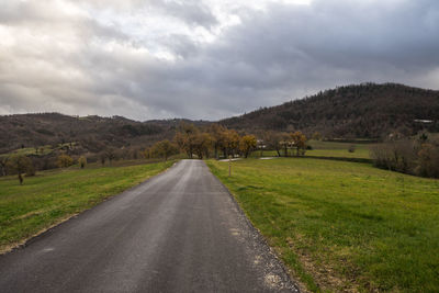 Empty road amidst field against sky