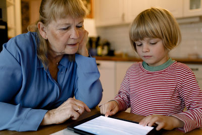 Senior woman looking at grandson using digital tablet