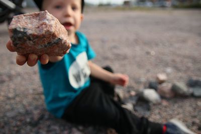 Close-up of boy holding rock while sitting on road