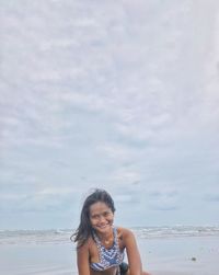 Portrait of smiling young woman standing at beach against sky