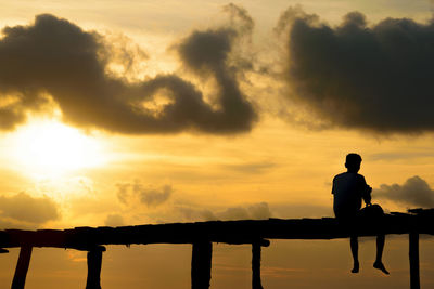 Man sitting on pier against sky during sunset