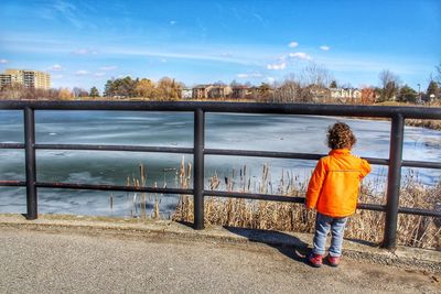 Rear view of boy standing by railing against sky