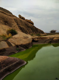 Rock formation by lake against sky