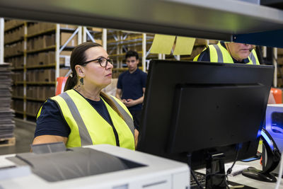 Confident mature female worker standing by coworker in distribution warehouse