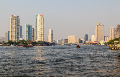 Sea and buildings in city against clear sky