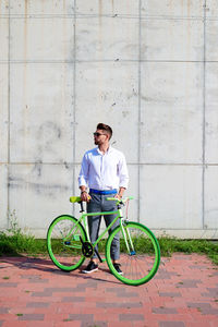 Young bearded man with sunglasses standing with bike outdoors