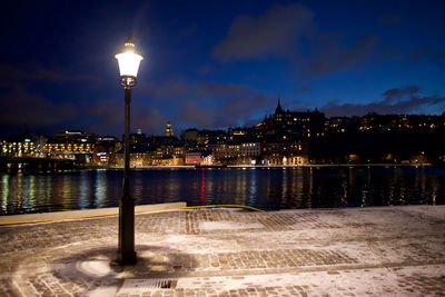 Illuminated city by river against sky at night