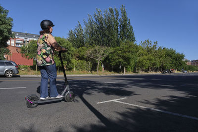 Side view of man riding push scooter on road