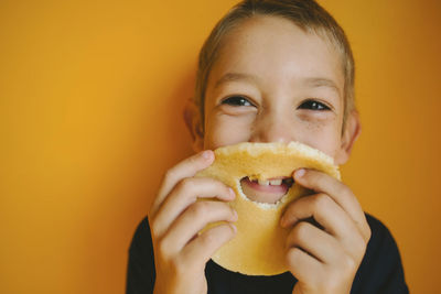 Happy boy looking away while holding bread with hole against orange wall at home